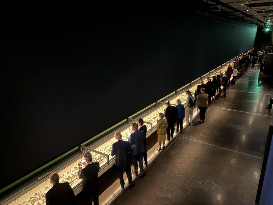 Visitors viewing the Bayeux Tapestry along the full length of the illuminated table showcase.