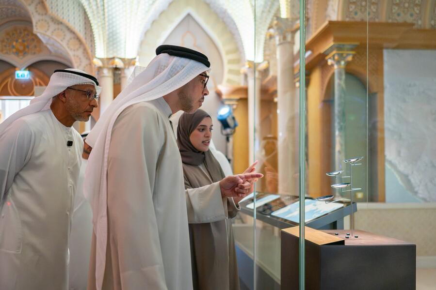 Visitors examining small objects presented in a freestanding glass museum showcase at Qasr Al Watan.