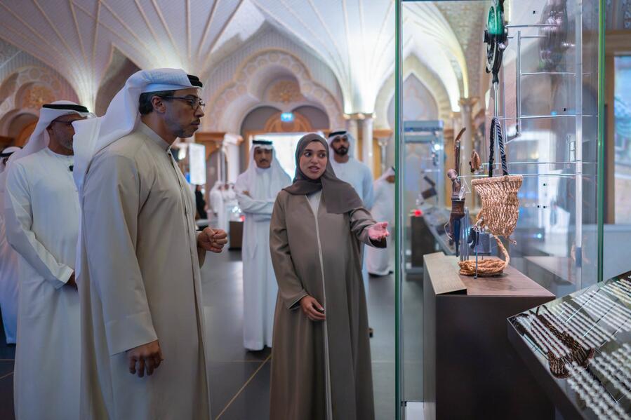Visitors beside a tall glass museum showcase displaying objects and woven items at Qasr Al Watan.